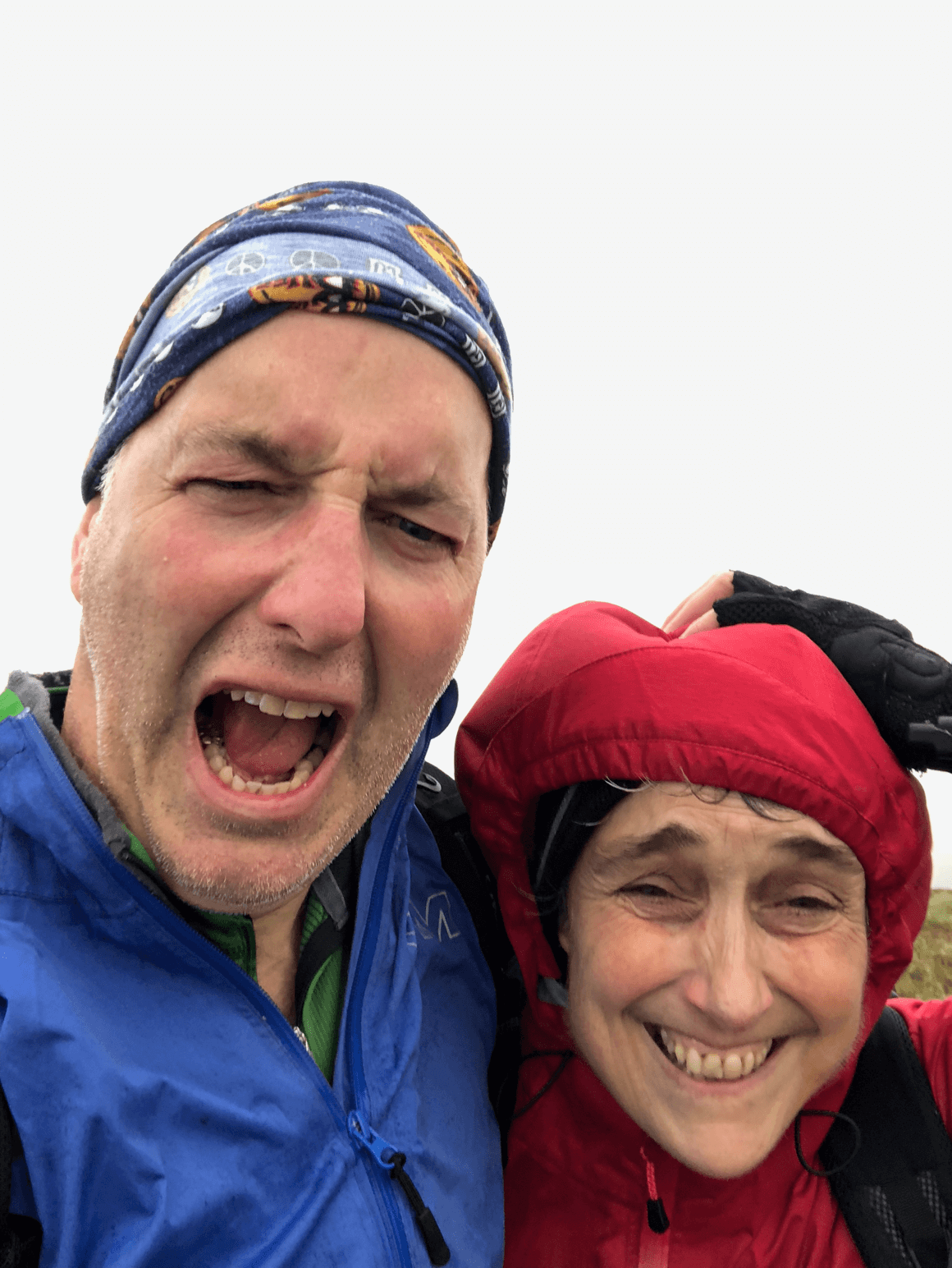 A man in blue and a woman in red, in heavy rain and wind, looking directly at the camera.