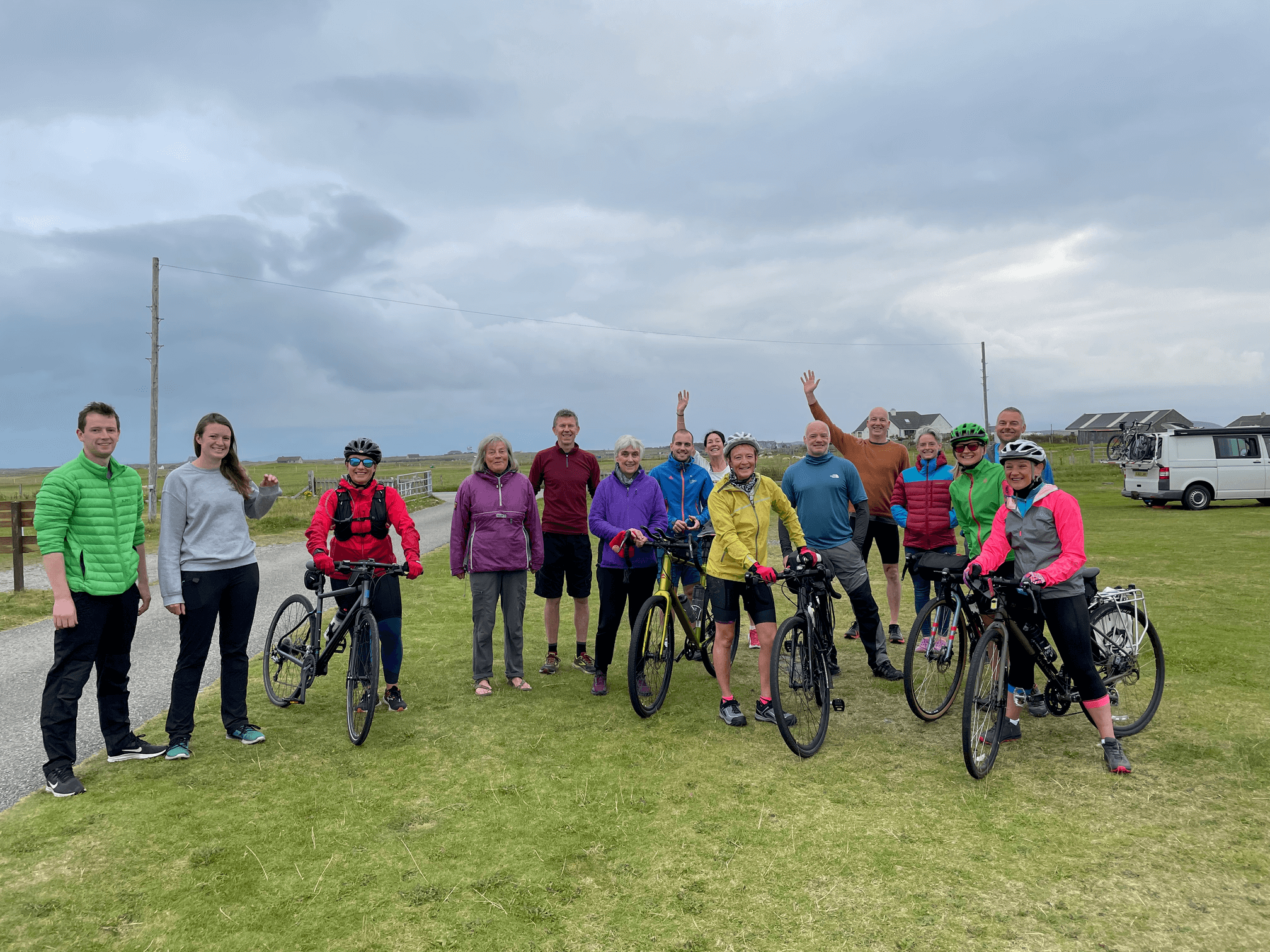A group of people standing in an almost empty campsite. Five people with bikes, the rest still getting ready.